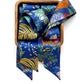 A vibrant liberty london silk twilly scarf with a multicolor tropical and floral print, neatly folded and presented inside a square wooden box against a plain white background.