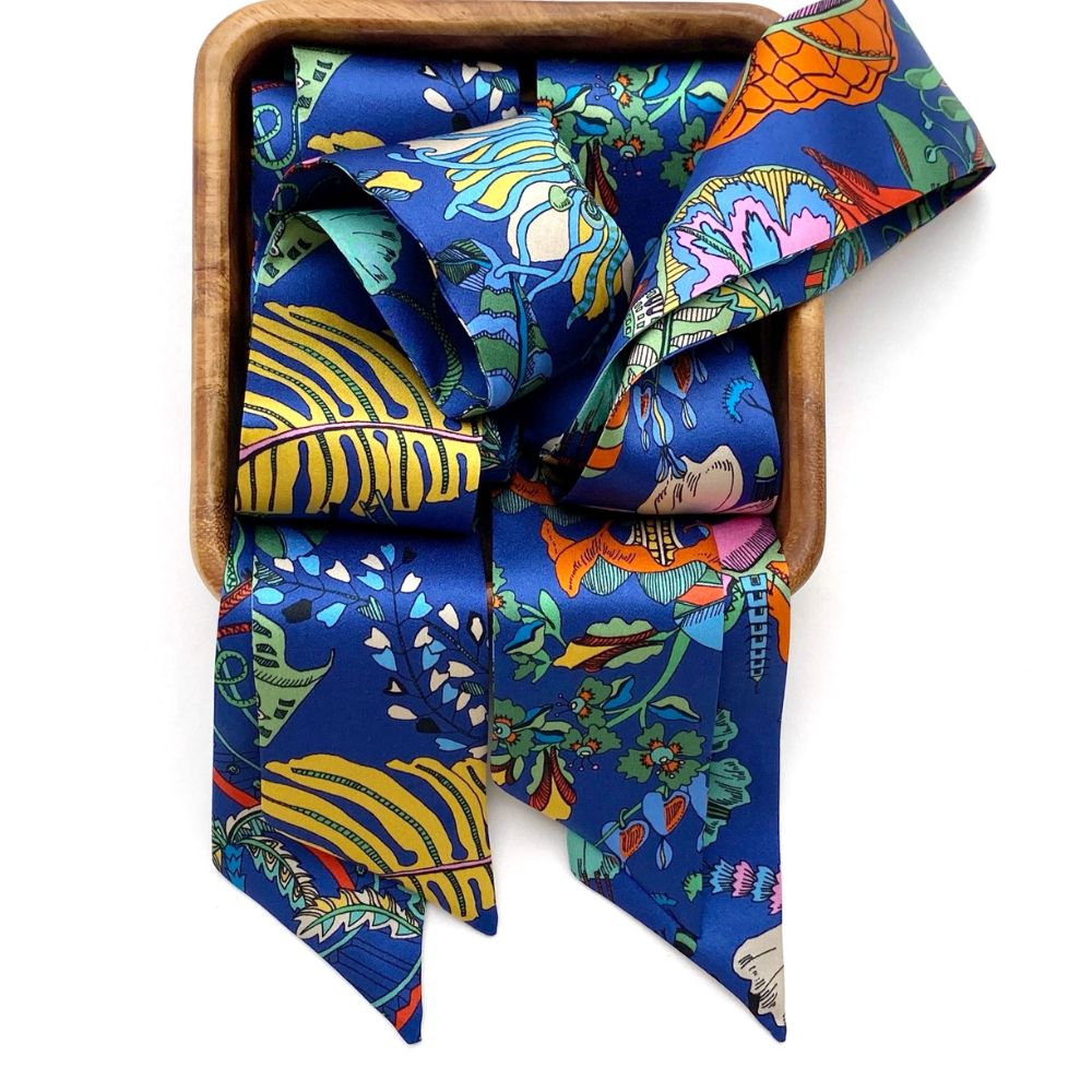 A vibrant liberty london silk twilly scarf with a multicolor tropical and floral print, neatly folded and presented inside a square wooden box against a plain white background.