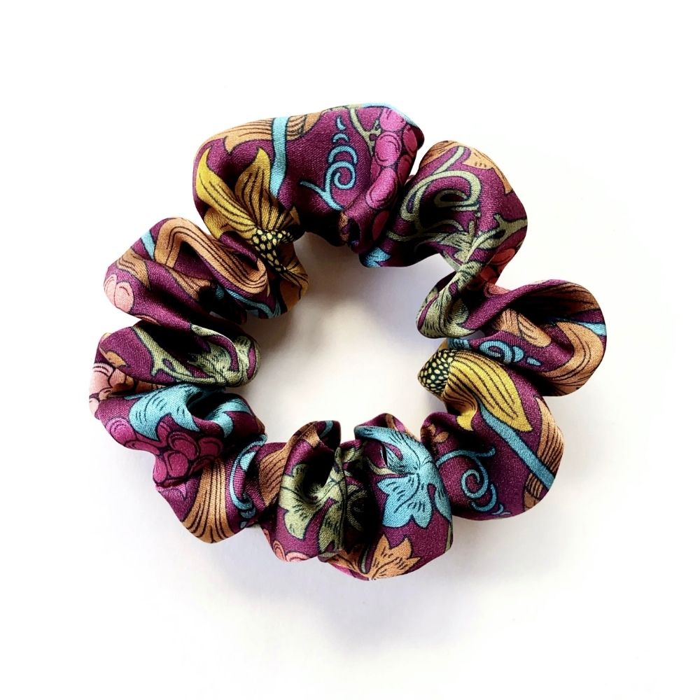 A liberty silk scrunchie with a multicolor paisley and floral pattern in purple, teal, yellow, and brown, shown on a plain white background.