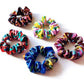 Five liberty silk hair scrunchies with colorful marbled and floral patterns in shades of blue, pink, yellow, red, and purple, arranged on a plain white background.