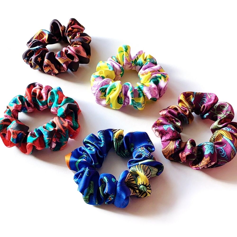 Five liberty silk hair scrunchies with colorful marbled and floral patterns in shades of blue, pink, yellow, red, and purple, arranged on a plain white background.