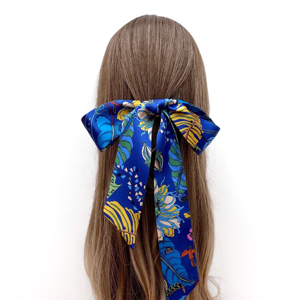 Blue Liberty silk skinny hair scarf tied in a bow on a person's head against a white background