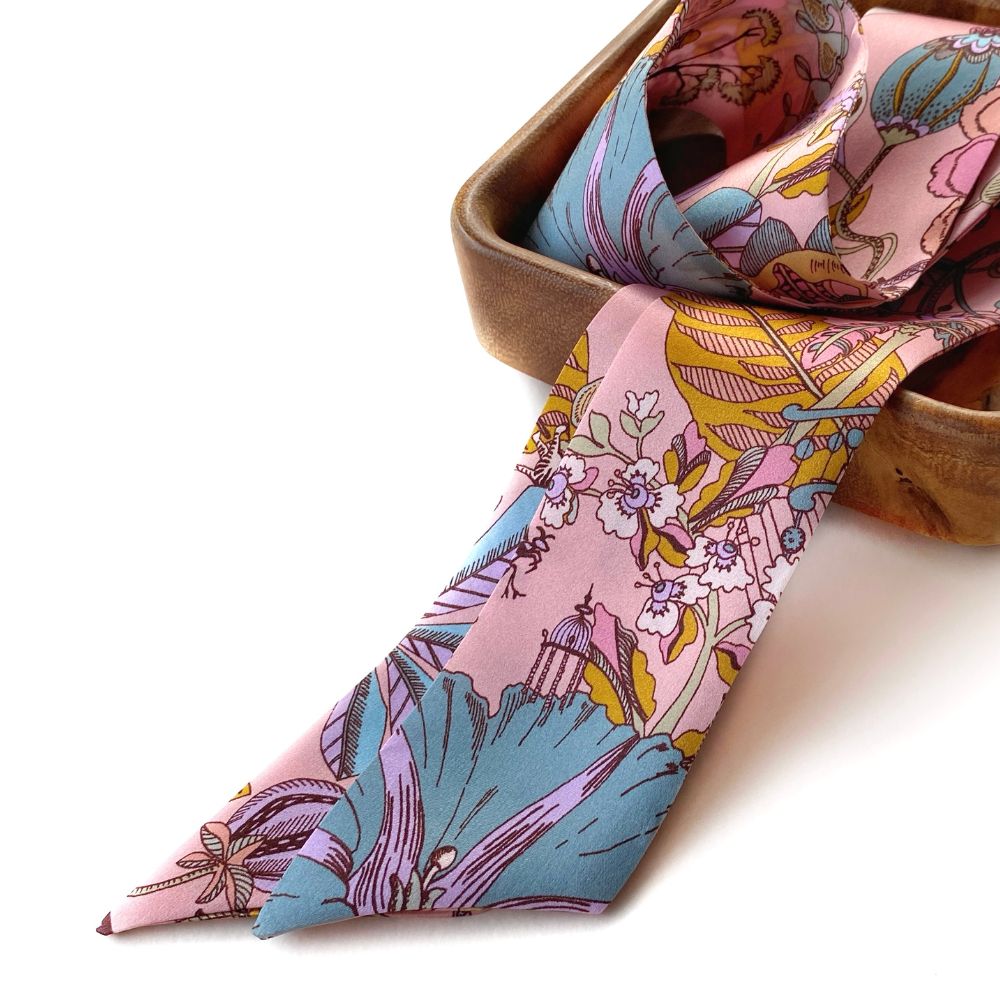 Pink Liberty silk skinny scarf draped over a wooden bowl on a white background