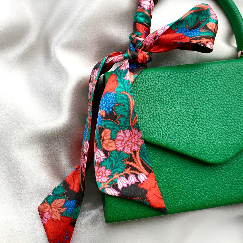Liberty silk twilly scarf wrapped and tied on a green handbag handle on a white background