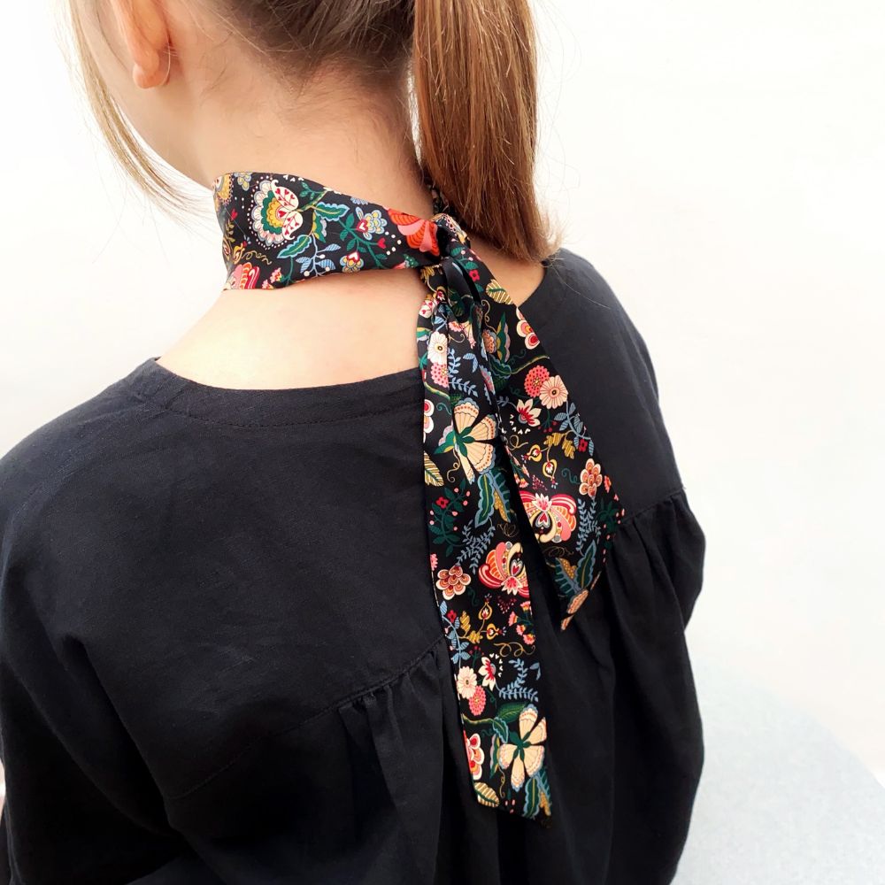 Person wearing a black liberty floral  print silk skinny necktie scarf against a white background
