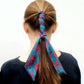 Person with a ponytail wrapped with a blue and pink floral Liberty silk skinny hair scarf against a white background