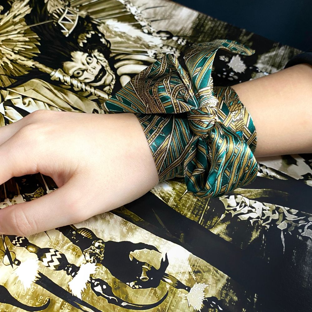 Hand wearing a liberty print silk skinny scarf as a bracelet on a decorative surface with intricate designs.