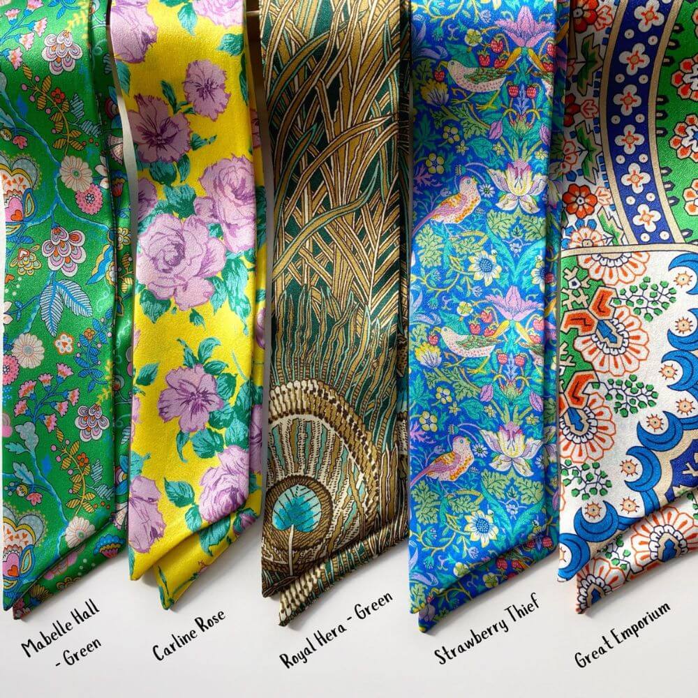 Collection of colorful patterned Liberty silk twilly scarves on a white background