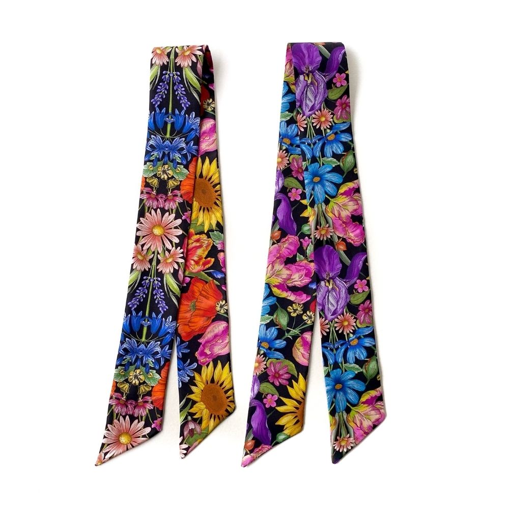 Two Liberty London silk twilly scarves with vibrant multicolor floral prints on a black background, displayed side-by-side against a plain white background.