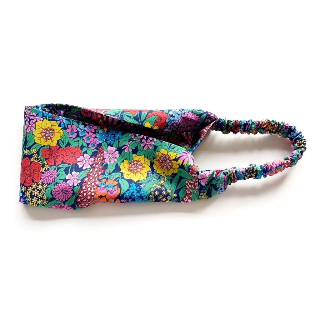 Liberty London Tana Lawn cotton headband with a vibrant multicolor floral print on a teal background, featuring a matching elastic back, photographed on a clean white background.