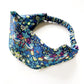A Liberty London Tana Lawn cotton headband with an elastic back, featuring william morris print " strawberry thief" a detailed floral and bird pattern in blue, green, pink, and yellow on a white background.
