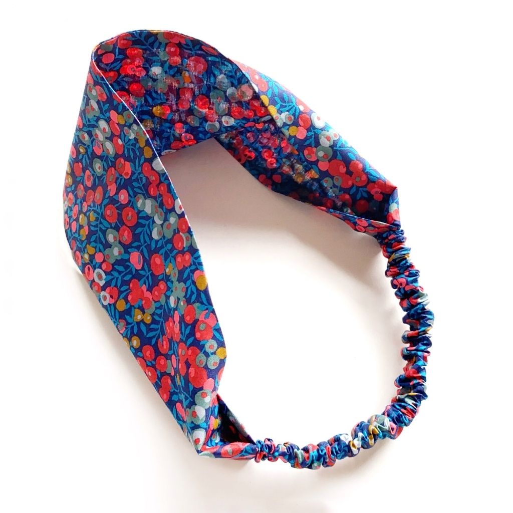 Liberty London Tana Lawn cotton  headband with a vibrant multicolor floral pattern on a blue background, featuring an elasticized back, shown on a plain white background.