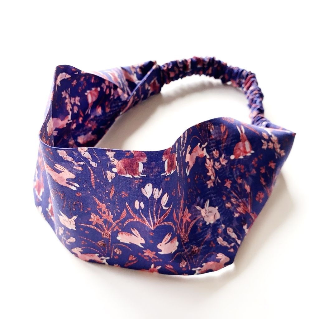 Liberty London Tana Lawn cotton headband, featuring a navy blue background with a pink and white rabbit and floral pattern, shown on a white background.
