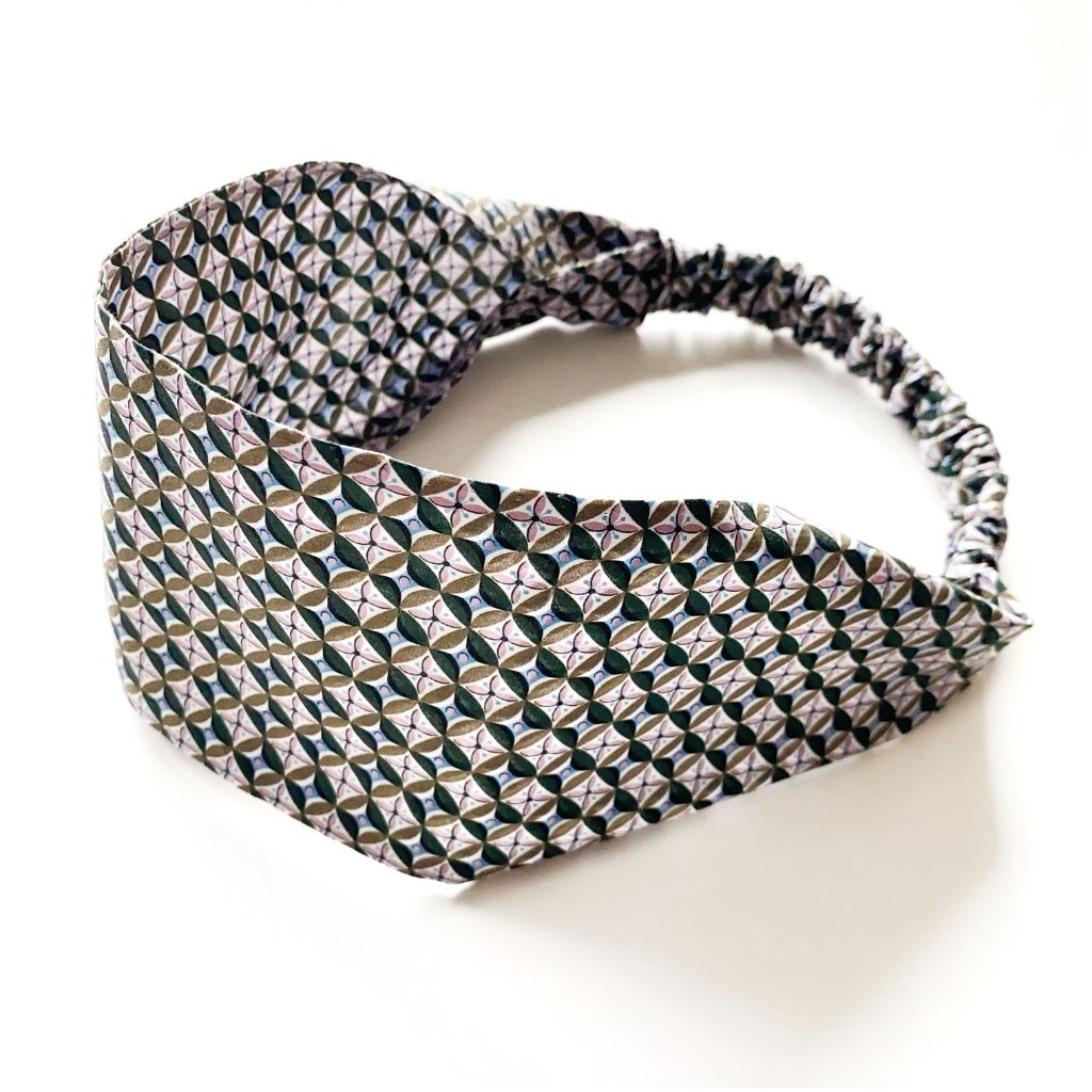 Liberty London Tana Lawn cotton headband with a geometric pattern of interlocking circles in black, white, and olive green, featuring an elasticized back band, shown on a plain white background.