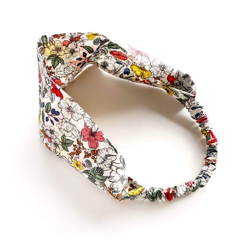 A Liberty London Tana Lawn cotton  headband, featuring a dense multicolor floral and botanical print on a white background, photographed on a clean white studio background.