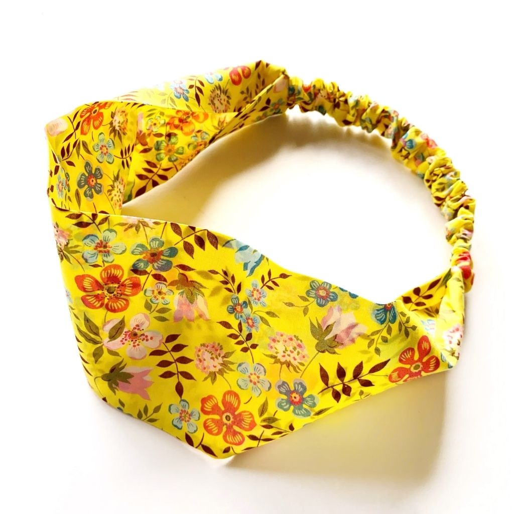 A yellow Liberty London Tana Lawn cotton  headband with a colorful floral print, featuring an elastic band, shown on a white background.