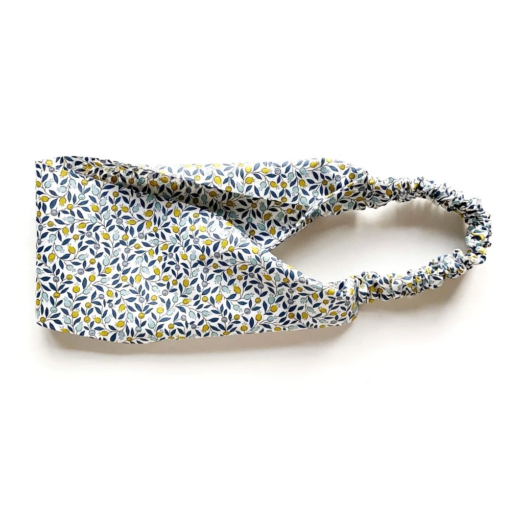 A Liberty London Tana Lawn cotton headband with a small yellow and blue floral pattern on a white background, featuring a gathered elastic band, photographed on a clean white surface.