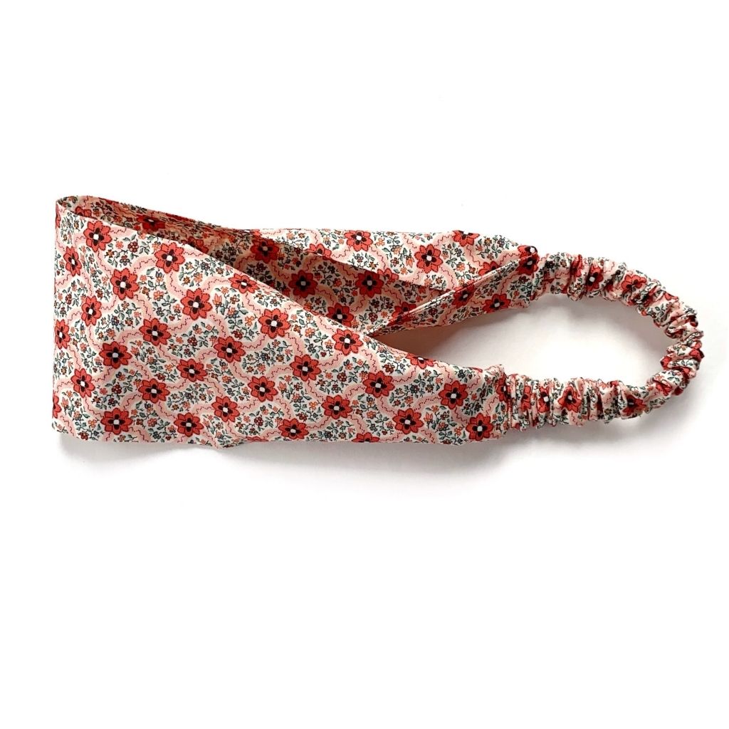 A Liberty London Tana Lawn cotton  headband with a small red floral pattern on a light beige background, featuring an elastic back, shown on a white background.