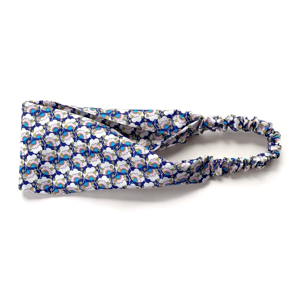 Liberty London Tana Lawn cotton headband with a blue, white, and gray floral pattern, featuring a gathered elastic back, shown on a plain white background.