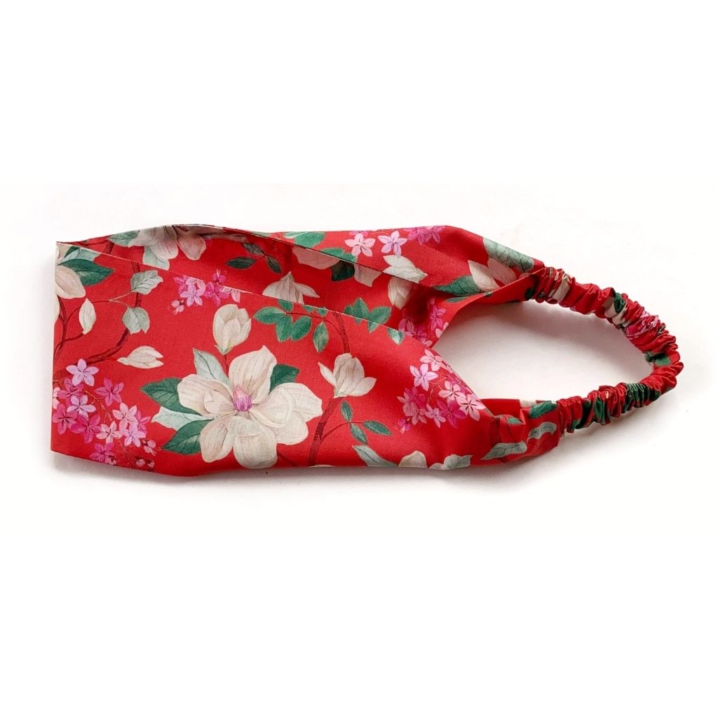 A orange red Liberty London Tana Lawn cotton headband with a white, pink, and green floral print, featuring an elastic band, shown on a plain white background.