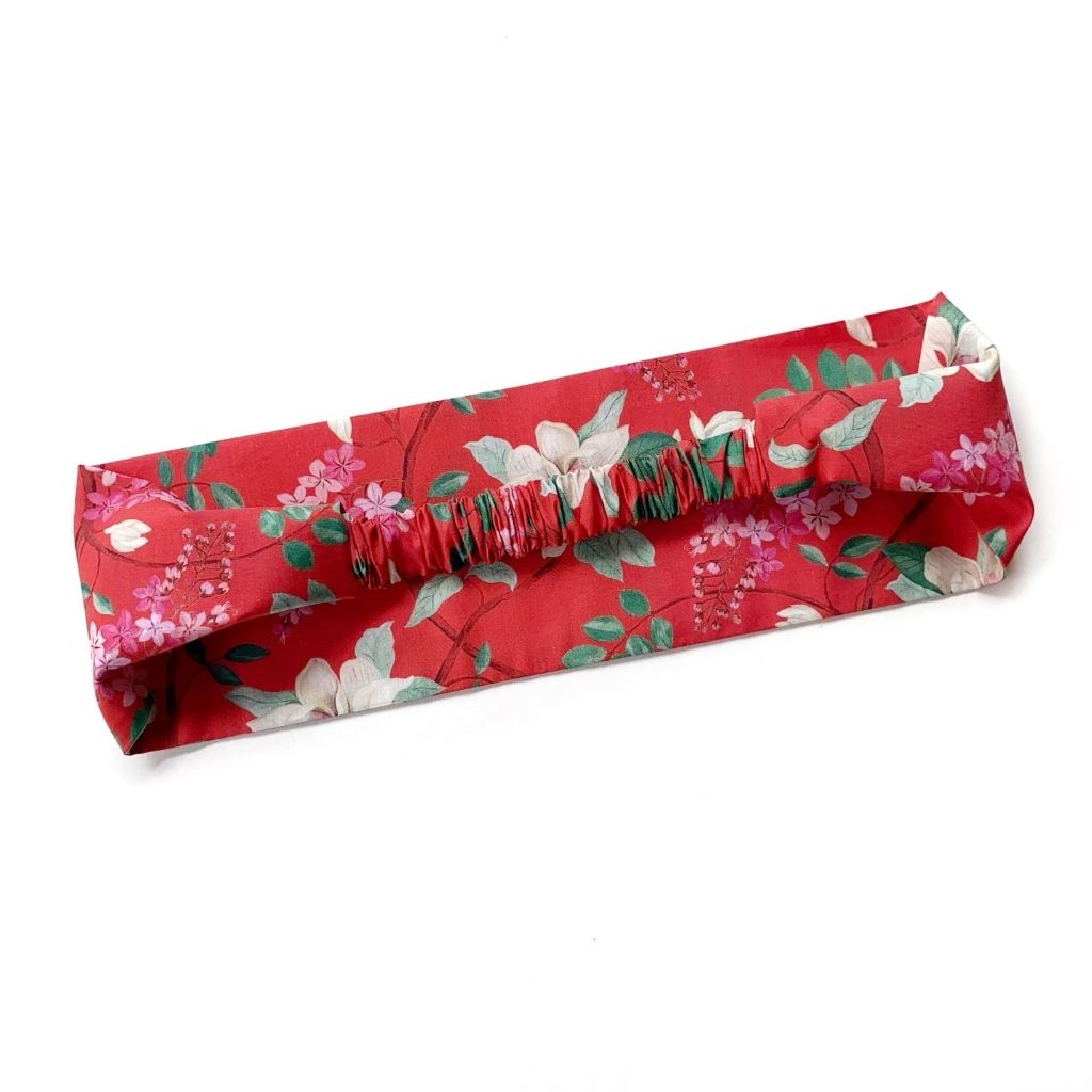 A red Liberty London Tana Lawn cotton  headband with a floral print of white and pink flowers and green leaves, featuring elastic band on the back, shown on a plain white background.