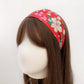 A orange red Liberty London Tana Lawn cotton headband with a floral pattern of pink and white flowers and green leaves, displayed on a mannequin head with long brown hair against a plain white background.