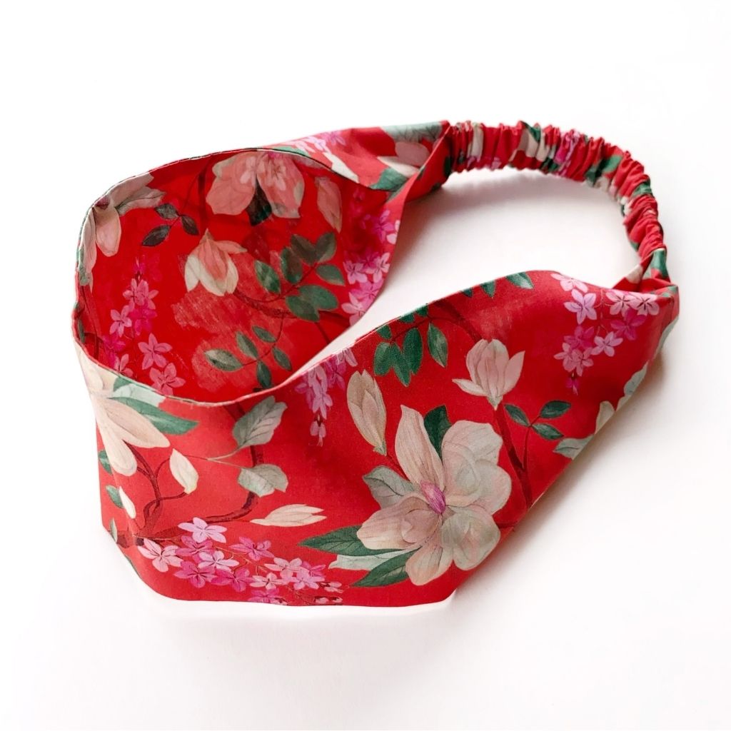 Orange red Liberty London Tana Lawn cotton headband with a floral print featuring large white and pink flowers and green leaves, shown on a plain white background.