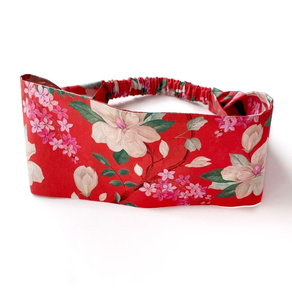 Liberty London Tana Lawn cotton  headband with an orange red background and a floral print featuring cream-colored flowers, pink blossoms, and green leaves, displayed on a clean white background.