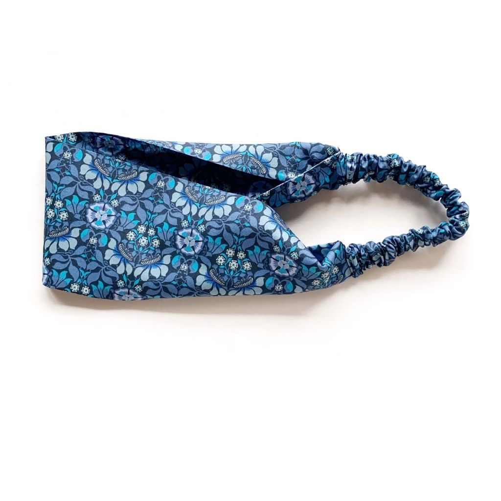 Liberty London Tana Lawn cotton headband with a blue and teal floral pattern, featuring a gathered elastic back, shown on a plain white background.