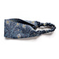 Liberty London Tana Lawn cotton headband with a dark blue and navy peacock feather pattern and gold accents, featuring a elastic band, shown on a white background.