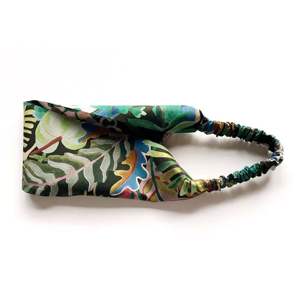 A Liberty London Tana Lawn cotton headband with a vibrant tropical leaf print in shades of green, blue, yellow, and orange, featuring a matching elasticated back, shown on a plain white background.