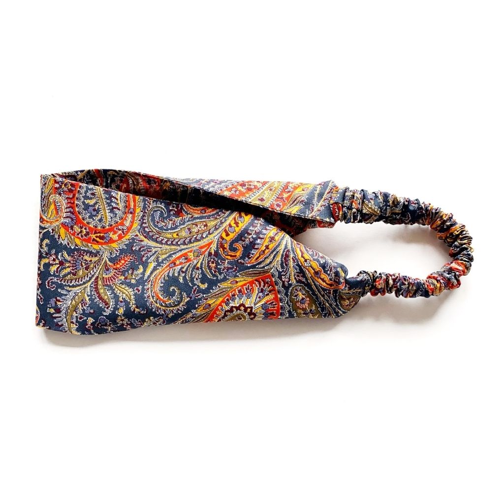 A Liberty London Tana Lawn cotton headband with a colorful paisley pattern on a navy blue background, featuring a gathered elastic band, shown on a plain white background.