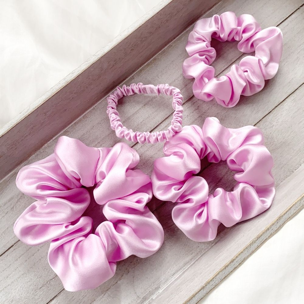 Set of lilac pure mulberry silk satin scrunchies and hair ties on a wooden surface