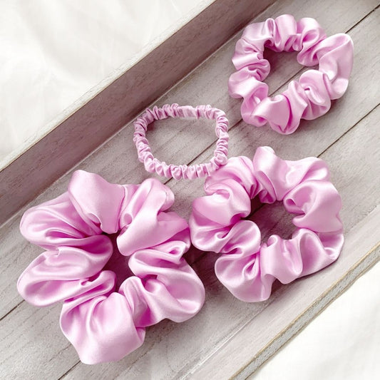 Set of lilac pure mulberry silk satin scrunchies and hair ties on a wooden surface