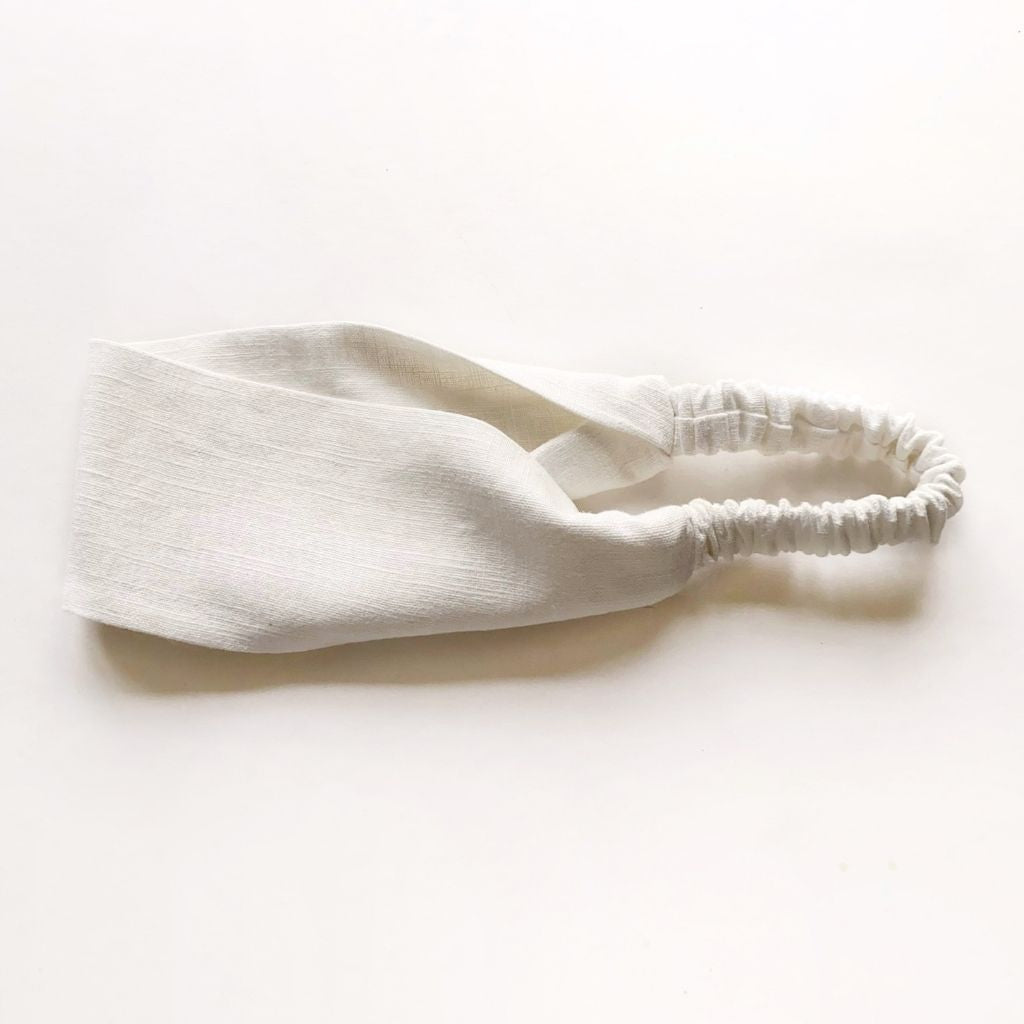 A ivory white linen headband with an elastic back, laid flat on a clean white background.