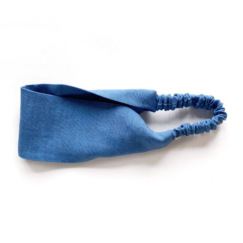 A denim blue flat linen headband with an elastic back, laid flat on a white background.
