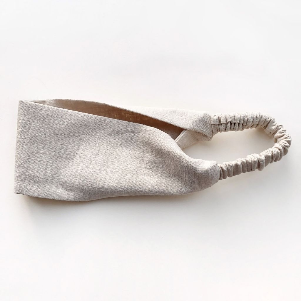 A light beige linen headband with a gathered elastic back, photographed on a clean white background.