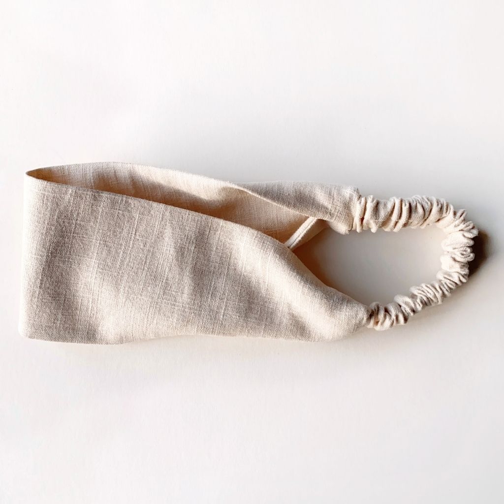 A light cream linen headband with an elastic back, displayed on a clean white background.