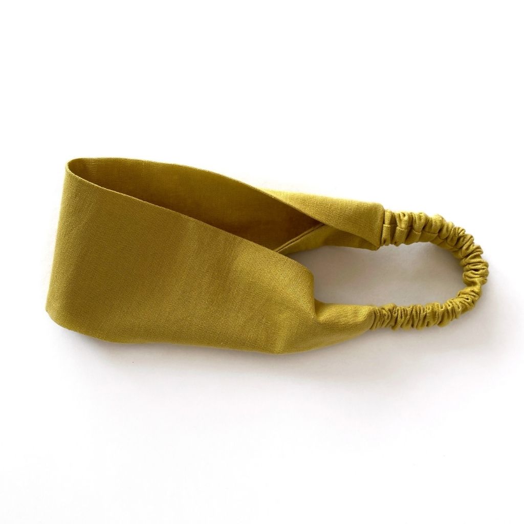 A mustard yellow flat linen headband with an elastic back, displayed on a clean white background.
