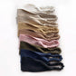 A set of linen headbands with elasticated ruffled ends, arranged in a vertical stack on a white background. The headbands come in multiple neutral and pastel colors, including ivory, cream, beige, tan, light pink, olive green, navy blue, and black.