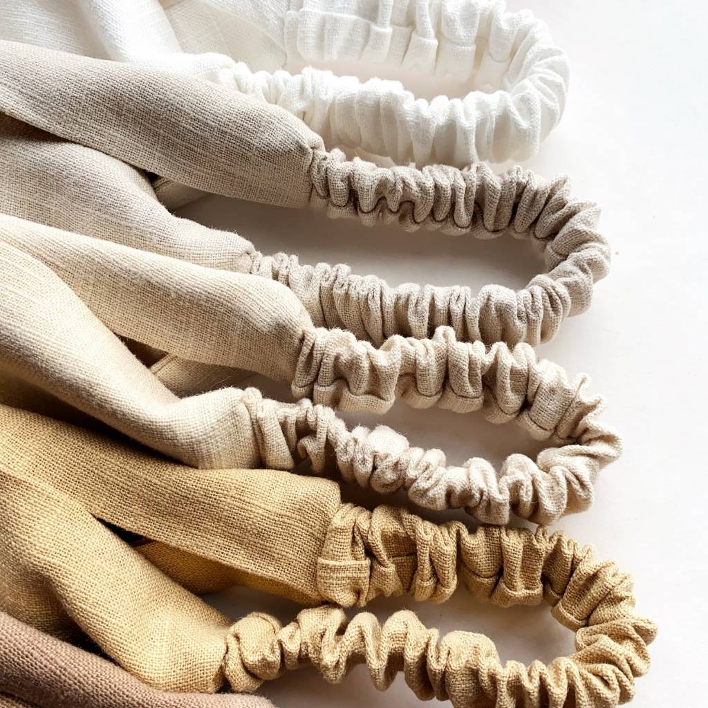 A close-up of several linen headbands  in soft neutral tones, arranged diagonally on a white background.