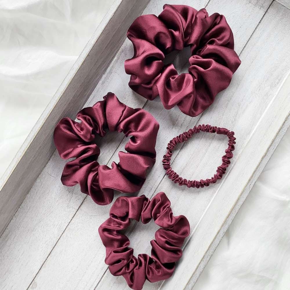 Set of maroon silk satin scrunchies on a light wooden surface