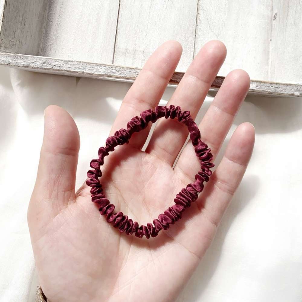 Maroon silk hair tie held in a hand on a light wooden surface