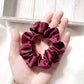 Maroon silk scrunchie held in a hand against a light wooden background