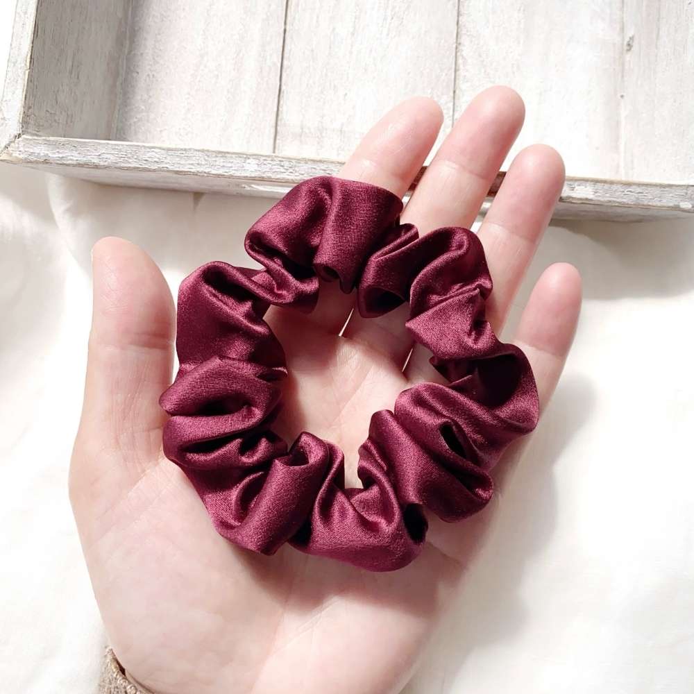 Maroon silk scrunchie held in a hand against a light wooden background