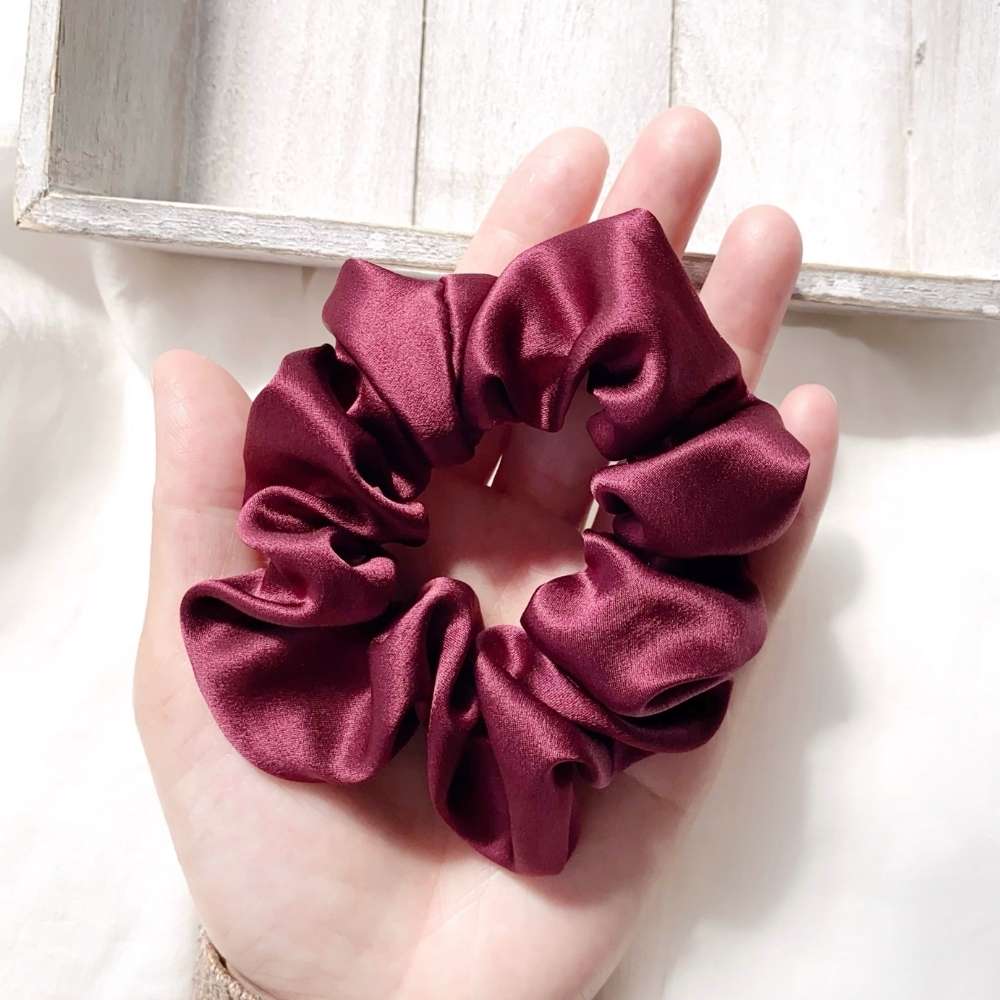Maroon silk satin scrunchie held in a hand against a light background