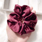 Maroon silk scrunchie held in a hand with a light background
