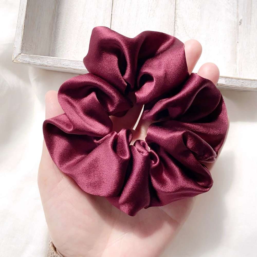 Maroon silk scrunchie held in a hand with a light background