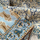 Detail shot of the mulberry silk and cotton blend bandana square scarf highlighting the teal and mustard paisley print and hand-rolled hem.