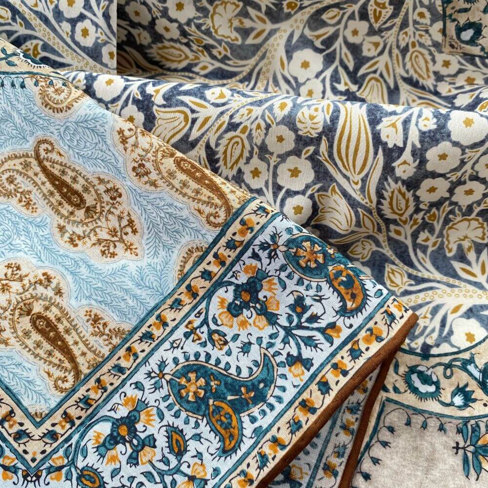 Detail shot of the mulberry silk and cotton blend bandana square scarf highlighting the teal and mustard paisley print and hand-rolled hem.